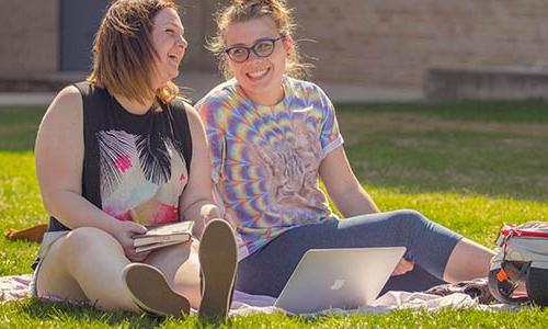 Two students sharing a laugh on Main Lawn while studying